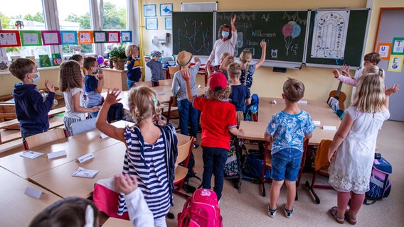 Schülerinnen und Schüler einer Grundschule stehen im Klassenzimmer vor ihren Plätzen. © picture alliance/dpa Foto: Jens Büttner
