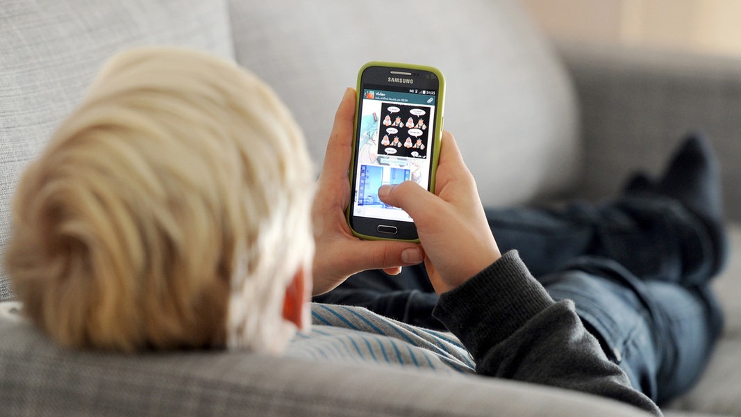 Ein Kind liegt mit einem Smartphone in der Hand auf einem Sofa.