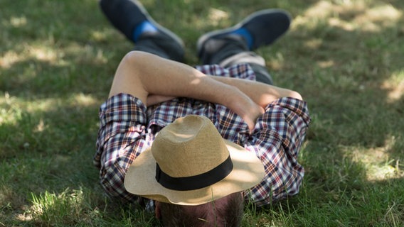 Ein Mann liegt mit einem Sonnenhut über dem Gesicht auf einer Wiese © picture alliance/dpa | Sebastian Kahnert Foto: Sebastian Kahnert