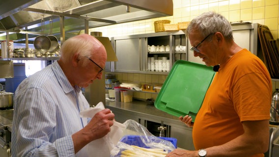 Spargelhof-Besitzer Carsten Oldenburg und Gasthof-Besitzer Karl-Heinz Märtens unterhalten sich über eine Kiste mit Spargel. © NDR 
