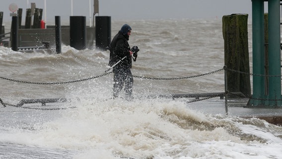 Ein Mann geht während des Orkans "Burglind" mit einem Fotoapparat auf einem Steg am Südstrand von Wilhelmshaven und wird von den Wellen getroffen. © picture alliance/dpa | Mohssen Assanimoghaddam Foto: Mohssen Assanimoghaddam