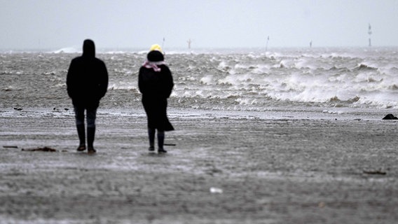 Spaziergänger gehen bei stürmischem Wetter an der Küste entlang. © picture alliance/dpa/Sina Schuldt Foto: Sina Schuldt