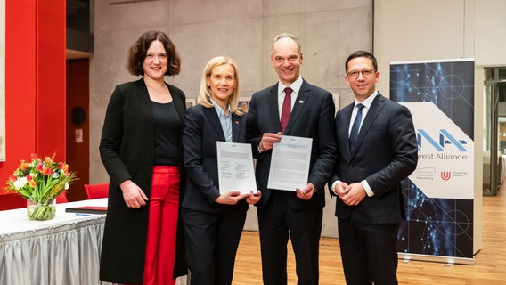 Um die Freude über die North West Alliance auszudrücken, stehen Kathrin Moosdorf (Senatorin für Klima, Umwelt und Wissenschaft der Freien Hansestadt Bremen), Jutta Günther (Rektorin der Universität Bremen), Ralph Bruder (Präsident der Universität Oldenburg) und Falko Mohrs (Niedersächsischer Minister für Wissenschaft und Kultur) nebeneinander. © Pressestelle der Universität Oldenburg Foto: Jens Oellermann