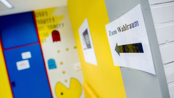 Ein Schild mit einem Pfeil und der Aufschrift "Zum Wahlraum" hängt in einem Wahllokal in der Hauptschule Damme. © dpa Foto: Hauke-Christian Dittrich