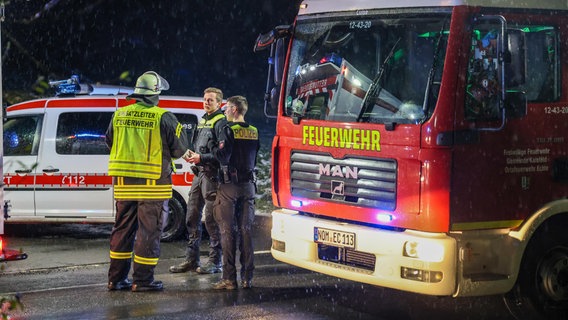 Zwei Polizisten und der Einsatzleiter der Feuerwehr zwischen einem Feuerwehrfahrzeug und einem Rettungswagen. © Kreisfeuerwehr Northeim Foto: Konstantin Mennecke