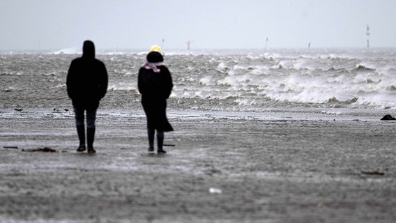 Spaziergänger gehen bei stürmischem Wetter durch das Watt vor dem Strand von Cuxhaven. © picture alliance/dpa Foto: Sina Schuldt