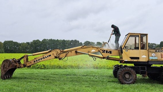 Ein Mann steht in der Wehrblecker Heide auf einem Bagger und wäscht ihn. © NDR Foto: Martina Spilker