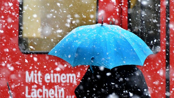 Eine Frau steht in Hannover bei Schneefall vor einer Straßenbahn mit der Aufschrift "Mit einem Lächeln...". © dpa Foto: Julian Stratenschulte