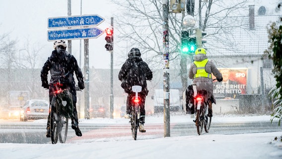 Radfahrer sind am Morgen im dichten Schneetreiben am Westkreuz im Oldenburger Stadtzentrum unterwegs. © dpa Foto: Hauke-Christian Dittrich