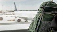 Ein Rucksack steht auf einem Flughafengelände. © IMAGO / Westend61 