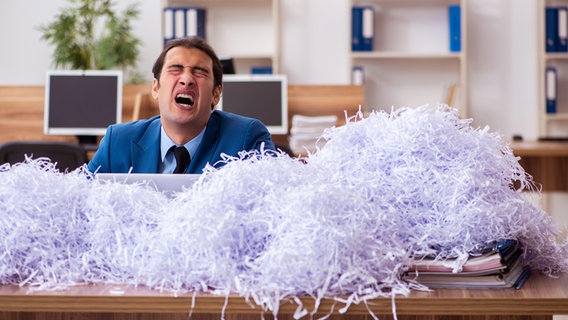 Ein Mann sitzt an einem Tisch voller geschreddertem Papier. © picture alliance / Zoonar Foto: Elnur Amikishiyev