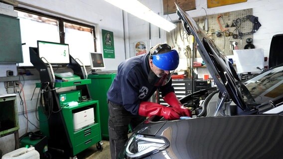 Ein Kfz-Mechatroniker arbeitet mit Insolierhandschuhen und Schutzhelm an einem E-Auto. © NDR Foto: Elin Halvorsen