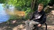 Finn Zielsdorf sitzt in seinem Rollstuhl an einem Ufer. © NDR Foto: Lena Haamann