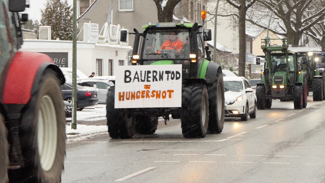 Ein Traktor fährt auf einer Straße, an ihm ist ein Schild montiert, auf diesem Steht: 