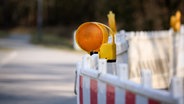 Ein weiß-roter Baustellenzaun mit einem Gelblichst steht an einer Straße. © NDR Foto: Pavel Stoyan