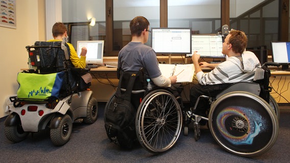 Drei Rollstuhlfahrer sitzen an einem Tisch und besprechen gemeinsam ihre Arbeit. © picture alliance Foto: Sebastian Willnow