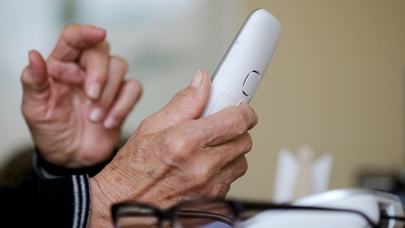 Ein alter Mensch hält ein weißes Telefon in der Hand. © picture alliance/dpa Foto: Roland Weihrauch