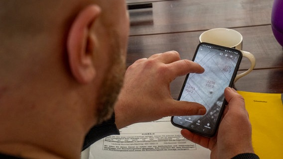 Fatih Onur schaut auf sein Handy - darin ein Foto von der Verdachtsstelle des Blindgängers. © NDR Foto: Thomas Viet Dang