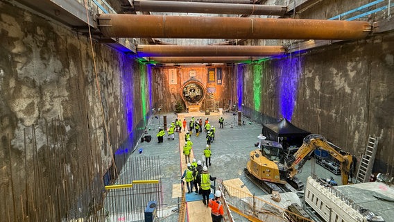 Ein Tunnel mit Rohren, Bauarbeitern und einem Bagger. © NDR Foto: Tobias Gellert