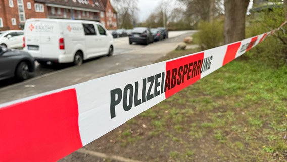 Ein rot-weißes Flatterband mit dem Schriftzug Polizeiabsperrung hängt zwischen Bäumen in Kiel-Elmschenhagen. © NDR Foto: Tobias Gellert