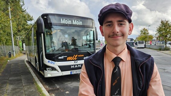 Ein junger Mann steht vor einem Bus und lächelt die Kamera. © NDR Foto: Johannes Tran