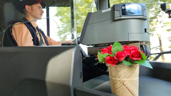 Ein junger Mann fährt einen Bus, im Vordergrund steht einige Blumen. © NDR Foto: Johannes Tran