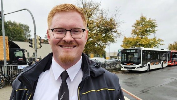 Ein junger Mann steht vor einem Bus und lächelt die Kamera. © NDR Foto: Johannes Tran