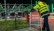 Ein Mann stellt ein Schild mit der Aufschrift "Warnstreik" auf vor dem Bushof auf. © dpa Foto: Bodo Marks