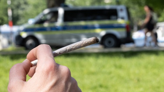 Eine Hand hält einen Joint, dahinter ein Polizeiauto. © picture alliance/dpa | Hannes P. Albert 