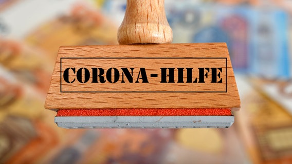 Ein Stempel mit der Aufschrift "Corona-Hilfe", im Hintergrund liegen viele Geldscheine. © picture alliance / Eibner-Pressefoto Foto: Weber/ Eibner-Pressefoto