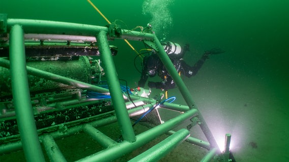 Ein Taucher schwimmt an einem Unterwasser-Observatorium auf dem Meeresgrund © GEOMAR Foto: Jan Duda