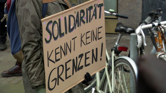 Eine Person hält ein selbst gemachtes Schild mit dem Schriftzug "Solidarität kennt keine Grenzen" bei einer Demo. © NDR 