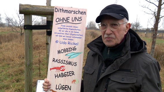 Ein Mann hält eine Texttafel in der Hand mit der Überschrift "Dithmarschen ohne uns". © NDR 