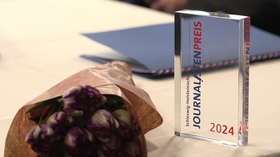 Der Siegelpokal für den journalistenpreis 2024 neben einem Blumenstauß © NDR Foto: NDR Screenshot