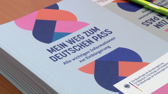 Ein Buch mit dem Titel "Mein Weg zum Deutschen Pass" liegt auf einem Tisch bei der Einbürgerungsbehörde Neumünster. © NDR 