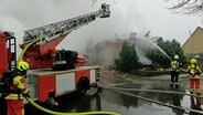 Einsatzkräfte der Feuerwehr löschen mit einem Feuerwehrschlauch ein Haus in Wohlde. © NDR 