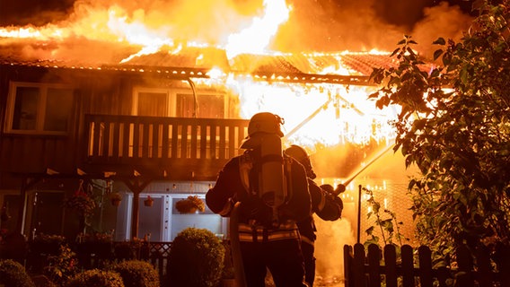Ein Feuerwehrmann steht vor einem brennenden Haus und sprüht Wasser aus einem Schlauch. © Kreisfeuerwehrverband Segeberg 