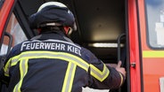 Schriftzug "Feuerwehr Kiel" ist auf der Uniform eines Feuerwehrmannes beim Einsteigen in ein Einsatzfahrzeug zu sehen. © NDR Foto: Pavel Stoyan