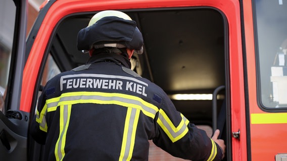 Schriftzug "Feuerwehr Kiel" ist auf der Uniform eines Feuerwehrmannes beim Einsteigen in ein Einsatzfahrzeug zu sehen. © NDR Foto: Pavel Stoyan