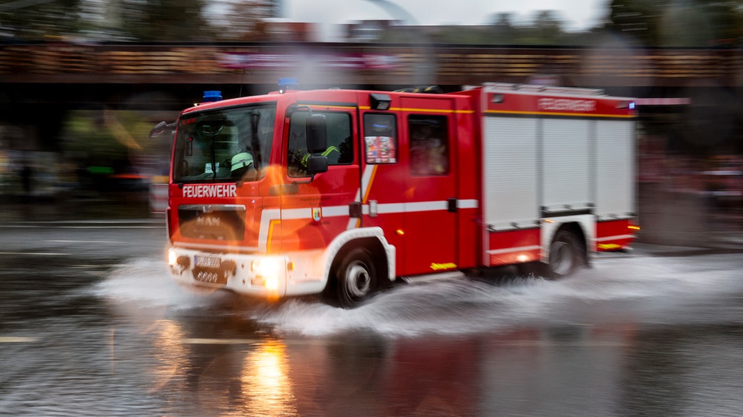 Ein Feuerwehrauto, welches um eine Kurve bei Regen fährt. 