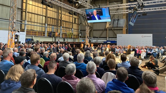 Viele Menschen sitzen auf Stühlen in der Werfthalle und schauen aufs Podium wo unter anderem Vizekanzler Robert Habeck sitzt. © NDR Foto: Simone Mischke
