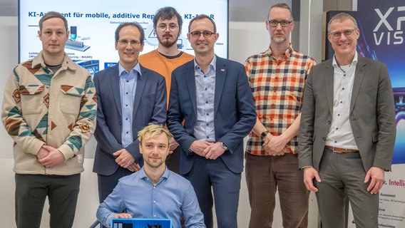 Philipp Schwarz (Projektmitarbeiter XRai Vision), Prof. Dr. Alexander Mattes (Projektleiter KI-AmaR), Erik Stölting (Projektmitarbeiter XRai Vision), Digitalisierungsminister Dirk Schrödter, Prof. Dr. Patrick Rupert-Kruse (Projektleiter XRai Vision), Prof. Dr. Björn Christensen (Präsident der FH Kiel), knieend: Laurin Vettel (Projektmitarbeiter KI-AmaR mit einem 3D-gedruckten Modell der Mobile Smart Factory) © F. Klein/FH Kiel Foto: F. Klein/FH Kiel