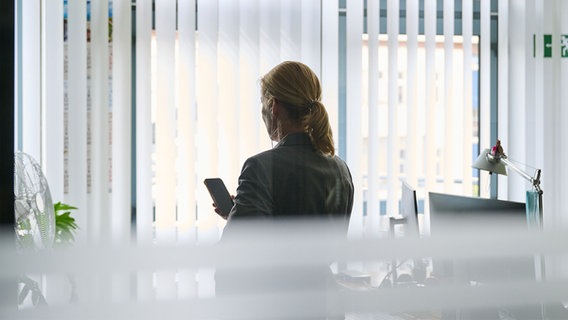 Eine Frau steht in einem Bürozimmer am Fenster und telefoniert über ein Headset. © picture alliance/dpa Foto: Annette Riedl