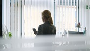 Eine Frau steht in einem Bürozimmer am Fenster und telefoniert über ein Headset. © picture alliance/dpa Foto: Annette Riedl