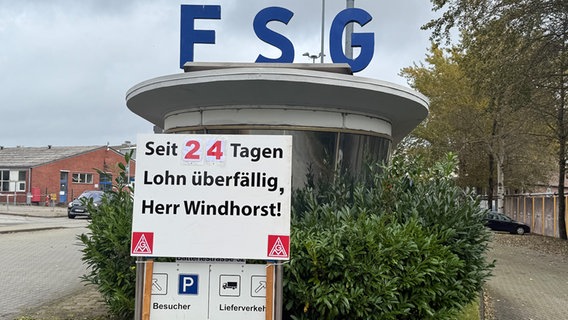 Der Eingang zur FSG-Werft in Flensburg, davor ein Schild mit der Aufschrift: "Seit 24 Tagen Lohn überfällig, Herr Windhorst!" © NDR Foto: Tobias Gellert