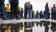 Mitarbeiter der Flensburger Schiffbau-Gesellschaft (FSG) warten auf das Statement von Ministerpräsident Günther bei einer Kundgebung nach einem Treffen mit Betriebsrat und Gewerkschaft IG-Metall auf dem Gelände der FSG. © picture alliance Foto: Christian Charisius