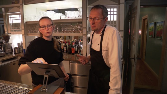 Hinter einem Tresen bespricht sich ein Restaurantbetreiber mit seiner Mitarbeiterin. © NDR 