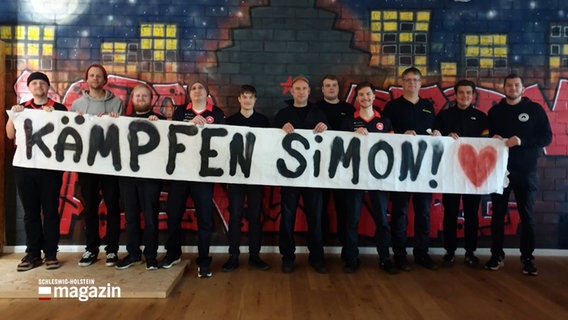 Eine Gruppe von Menschen hält ein Banner in der Hand mit der Aufschrift "Kämpfen Simon!". © NDR 