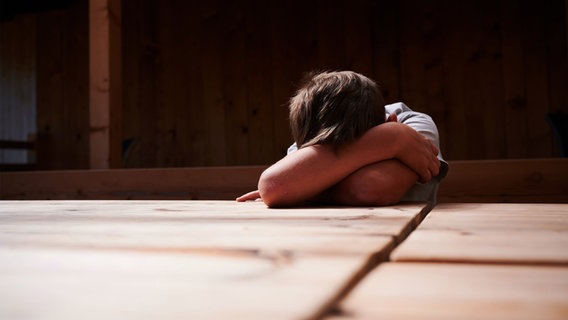 Ein Kind versteckt sein Gesicht unter seinen Armen und liegt mit dem Kopf auf einem Tisch. © dpa Foto: Annette Riedl