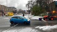 Ein blaues Auto fährt durch eine verschneite Innenstadt, im Hintergrund fährt ein Streuwagen. © NDR 